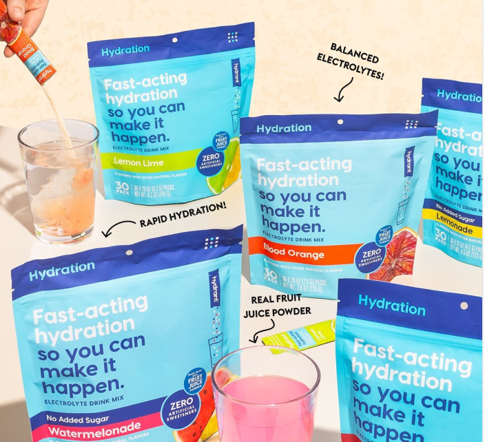 Assorted flavored electrolyte drink mix packets and glasses with mixed drinks on a table.